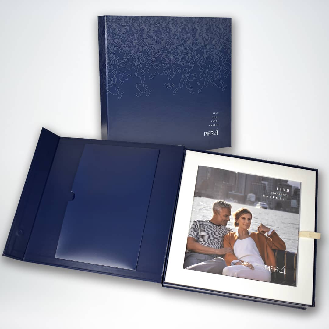 Two navy blue presentation folders with texture designs lying open, one displaying a brochure featuring a person couple by the water. The text reads "PIER4."
